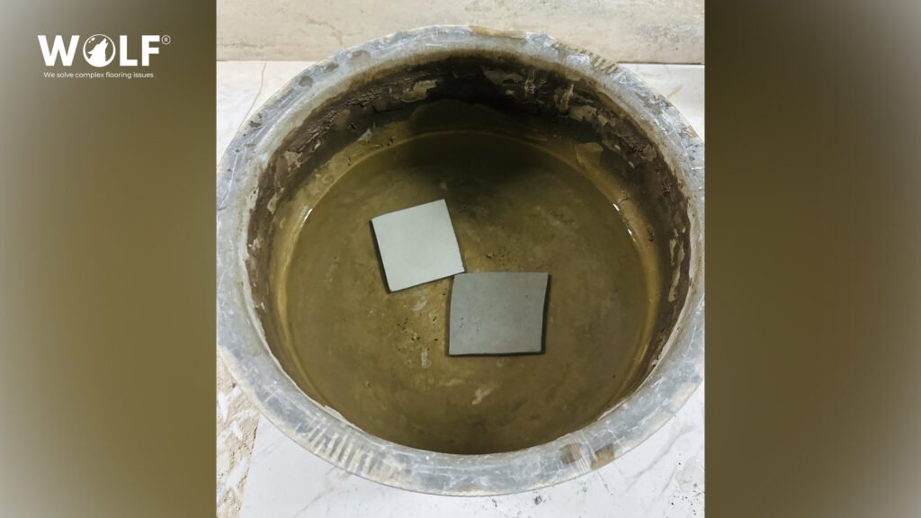 Two porcelain tile samples soaking in water in a metal bowl for a basic water absorption check